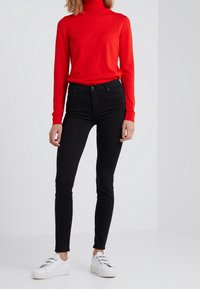 Röd polotröja, åtsittande svarta jeans och vita sneakers med snörning. Släta texturer, smal form och kontrast i färger.