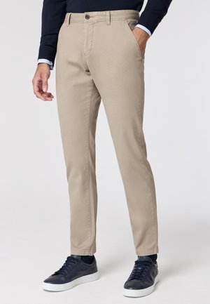 Beige trousers made of cotton blend, featuring a straight cut, front pockets, a button closure, and styled with navy sneakers.