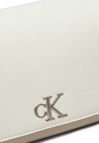 A pouch in pelle bianca in texture con una finitura liscia, caratterizzata da un logo "cK" in argento nell'angolo e un bordo beige a contrasto.