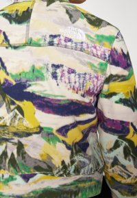 Fleecepullover med ett flerfärgat abstrakt bergsmönster i nyanser av gult, grönt, lila och svart. Broderad logotyp på ryggen.