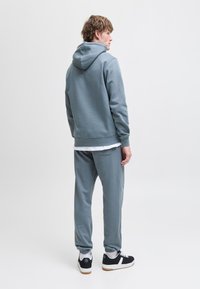 Hætte sweatshirt og sweatpants i dæmpet blågrå stof. Sweatshirten har en afslappet pasform; bukserne har elastiske mansjetter. Sorte sneakers fuldender looket.