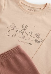 Kortærmet beige t-shirt med kaninprint og teksten "hop-hop-jump". Blødt stof, parret med pink bukser med elastisk talje.