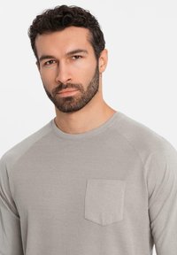 Hellgrau long-sleeve Shirt mit gerippter Textur, ausgestattet mit einem runden Ausschnitt und einer Brusttasche. Entworfen mit Raglanärmeln.