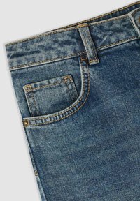 Dżinsy w średnim niebieskim odcieniu, z klasycznym pięciopocketowym wzorem, kontrastowym pomarańczowym przeszyciem i gładką teksturą z lekkim wyblaknięciem.