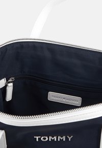 Marinblå tygväska med vit dragkedja och handtag. Har en dragkedjeinnerficka och en logotagg i grått läder. Slät textur.