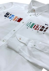 Camisa blanca de botones con logotipos impresos coloridos en rojo, azul y verde. Incluye detalles de botones en azul y rojo, con una textura de tela suave.