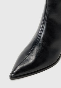 Mustat tekonahka ankle-bootit, joissa on terävä kärki, tyylikäs pinta ja kapea korko. Sivussa on pystysuoraa ommelta lisäyksinä.
