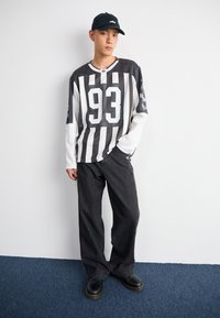 Mustvalge triibuline pikavarrukaline särk number 93, millele on sobitatud laiad tumedad teksased ja mustad puusatsid. Tumedast värvist müts lõpetab välimuse.