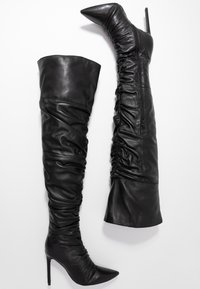 Schwarzlederne Overknee-Stiefel mit spitz zulaufenden Zehen, hohen Stiletto-Absätzen und geraffter Textur. Verfügt über einen seitlichen Reißverschluss zur Schließung.