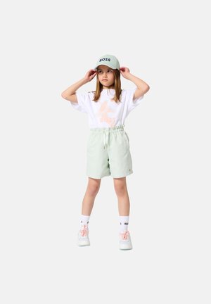 T-shirt blanc avec graphique "BOSS" rose, short vert clair avec taille élastique, casquette menthe avec "BOSS", chaussettes blanches et baskets pastel.