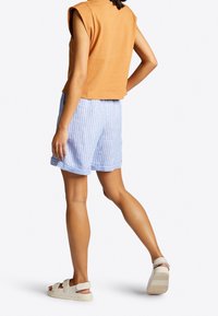 Orange ærmeløs top, der er parret med blå og hvide stribede shorts. Shortsene har en afslappet pasform og rullede manchetter, og de bæres med lyse sandaler.