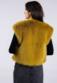 Faux-Fur-Weste in leuchtendem Gelb mit plüschiger Textur, ärmellosem Design und einem schwarzen, taillierten Top darunter. Schwarzer Jeansrock mit Taschen.