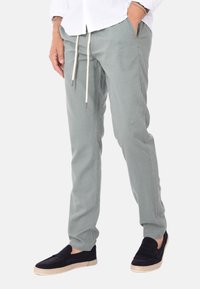 Pantaloni in cotone verde chiaro con vita elasticizzata e tasche laterali, abbinati a scarpe nere senza lacci con suola in juta.