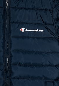 Tmavě modrá prošívaná péřová bunda s předním zipem a bílým logem "Champion" na hrudi. Hladká textura.