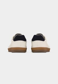 Coppia di sneakers bianche basse con suole in gomma e inserti blu scuro sul tallone, viste da dietro su uno sfondo semplice.