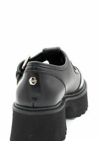 Zwarte leren schoen met een dikke platformzool, voorzien van een zilveren hexagonaal logo aan de achterkant en een ronde tekening.