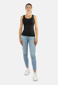 Schwarzes ärmelloses Tanktop aus glattem Stoff, kombiniert mit hellblauen enganliegenden Jeans und weißen Sneakers.