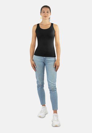 Schwarzes ärmelloses Tanktop aus glattem Stoff, kombiniert mit hellblauen enganliegenden Jeans und weißen Sneakers.