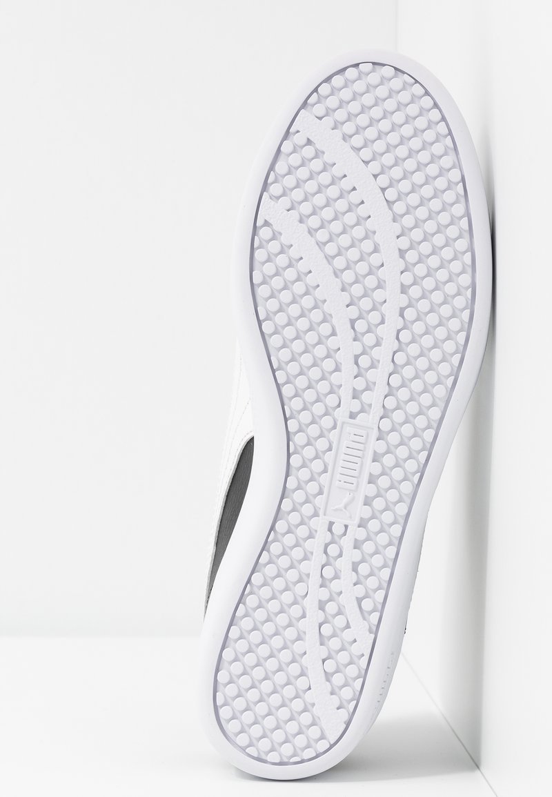 Suela de zapatilla blanca con grip circular texturizado y logo de Puma en relieve, centrado sobre un fondo blanco limpio.