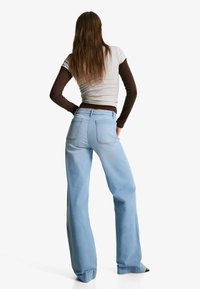 Svetlo modre zvonaste jeans hlače z visokim pasom, petimi žepi in subtilnimi šivi, kombinirane s prilegajočo sivo-rjavo majico z dolgimi rokavi.