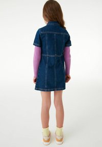 Rienshortsivar denim knælængde med krave og korte ærmer, parret med en langærmet pink top under og farverige sneakers.