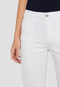 Weiße Denim-Jeans im Slim-Fit, mit Fronttaschen, Reißverschluss und einem sichtbaren Metallknopf am Bund. Glatte Textur.