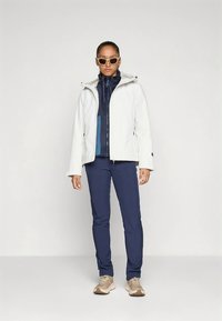 White waterproof jacket with a navy inner layer, paired with navy pants and light tan sneakers. Includes a hood and zippered pockets.