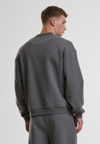 Felpa grigia con colletto a giro, vestibilità leggermente oversize e polsini a coste. Il tessuto ha una texture liscia senza motivi o accenti visibili.