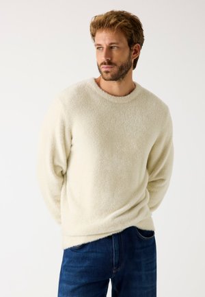 Suéter de forro polar color crema claro con cuello redondo y mangas largas, combinado con jeans azul oscuro. Textura suave y corte relajado.