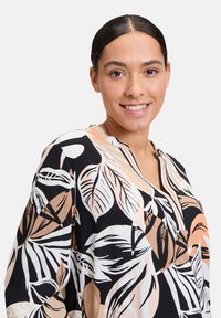 Czarna bluzka w kwiatowy wzór w odcieniach beżu, brzoskwini i bieli. Posiada dekolt w serek i długie rękawy, wykonana z lekkiego materiału.