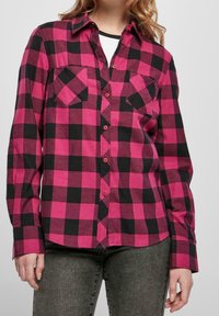 Rosa och svart rutigt långärmad skjorta med knäppning fram, två bröstfickor och en rundad nederkant. Tillverkad av ett strukturerat, vävt tyg.