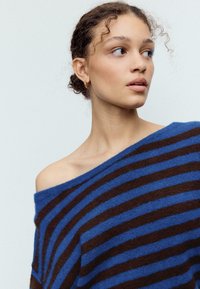 Modrý a hnedý pásikavý pletený sveter s odhalenými ramenami a jemnou textúrou, s širokými horizontálnymi pásikmi a pohodlným strihom.