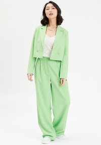 Groene cropped blazer, gecombineerd met losse, hooggewaagde broek. Textured wit topje eronder. Losse, zachte stof en sluiting met twee knopen.
