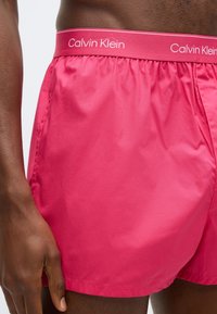 Ροζ μαγιό σορτς Calvin Klein με απαλή υφή, ελαστική μέση και λωρίδα με λογότυπο αντίθετου χρώματος. Ορατές λεπτομέρειες στην πλαϊνή ραφή.