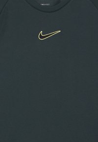 Fekete Nike Dri-FIT póló, sárgával körvonalazott fekete Nike swoosh logóval, középen a gallér alatt.