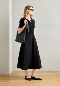 Black cotton dress with short sleeves and button detail, paired with black slingback flats and a black tote bag. Smooth texture, flowy silhouette.