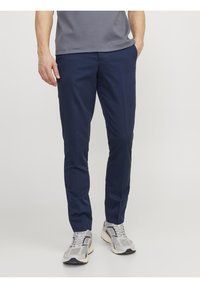 Marinblå slim-fit byxor i mjukt tyg, med framfickor och platt framsida. Bärs med grå sportskor.