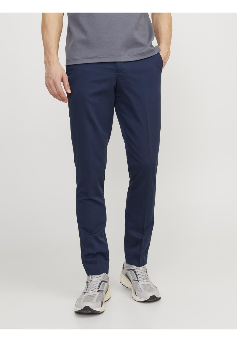 Marinblå slim-fit byxor i mjukt tyg, med framfickor och platt framsida. Bärs med grå sportskor.