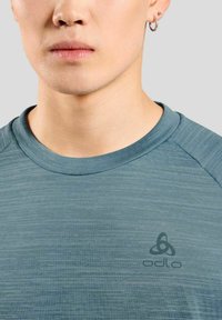 Grijsblauwe Odlo t-shirt met ronde hals, gestructureerde stof en klein logo op de borst. Glad afwerking met raglanmouwen.