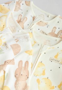 Tre bebiskläder gjorda av mjukt, ribbat tyg. Färgerna inkluderar krämfärgad, mjuk gul och ljusbrun med mönster av kanin och kyckling.