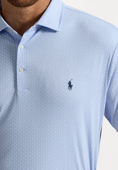 Polo azul claro com pequeno padrão branco, dois botões fechados e logótipo de jogador de polo bordado em azul escuro no peito.