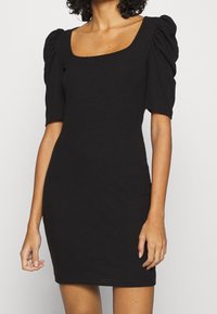 Černé žebrované šaty s čtvercovým výstřihem, krátkými nabíranými rukávy a přiléhavým střihem, vyrobené z elastického materiálu.