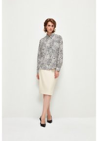 Schwarz-weiße Leopardenmuster-Bluse mit Kragen und langen Ärmeln, kombiniert mit einem cremefarbenen Bleistiftrock und schwarzen High Heels.