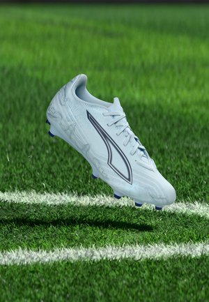 White soccer cleat with black logo floating above green grass near white boundary line on a sports field.