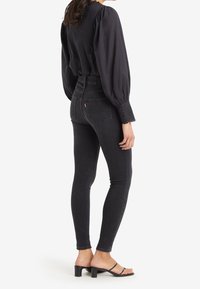 Jeans ajustados de tiro alto en negro con un corte elegante, complementados por una blusa negra estructurada con mangas abullonadas y detalles de botones.