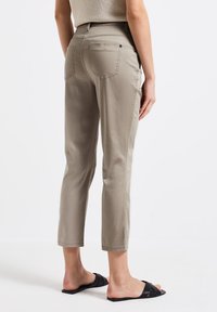 Pantalons cropped beiges en tissu doux, dotés de deux poches arrière et d'une coupe droite, associés à des sandales noires à glissière.