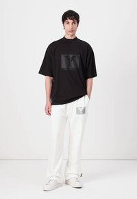 Zwarte T-shirt met korte mouwen en een grafische print op de borst, gecombineerd met witte sweatpants met een logo-label en een relaxte pasvorm.