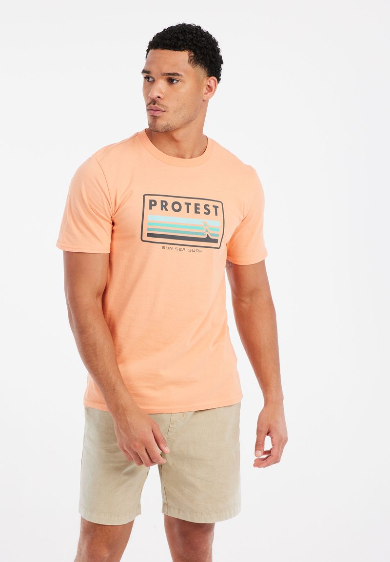 Šviesiai oranžinė marškinė su juodu ir žalia "PROTEST" logotipu bei bangų grafika; apvaliu iškirpimu; dėvimi su smėlio spalvos šortais; pagaminti iš medvilnės.