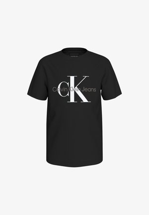 Črna bombažna majica s kratkimi rokavi, ki prikazuje velik bel logotip "CK" in besedilo "Calvin Klein Jeans" spodaj. Ima okroglo ovratnico.