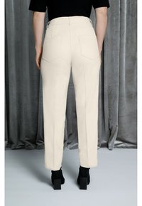 Béžové kalhoty na míru s vysokým pasem, obsahující dvě zadní kapsy a rovný střih nohavic, doplněné černými lodičkami na vysokém podpatku.